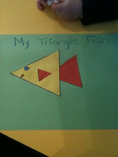 a child's hand writing on a piece of paper that says, my triangle fish