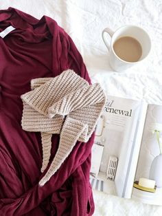 a sweater and hat laying on top of a bed next to a cup of coffee