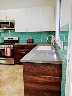 a kitchen with white cabinets and green tile backsplashing, stainless steel appliances