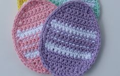 four crocheted coasters in different colors on a white surface with one painted yellow, the other pink