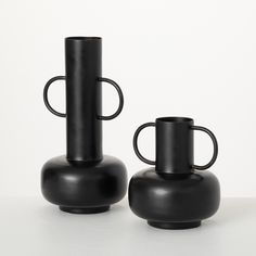 two black vases sitting next to each other on a table