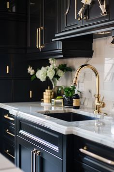 a kitchen with black cabinets and white marble counter tops, gold faucets and brass accents