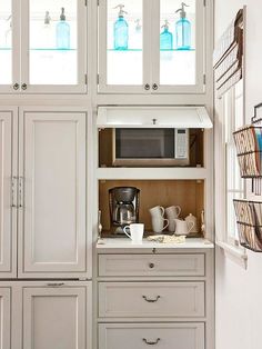 a kitchen with white cupboards and glass front cabinets in the corner, including a coffee maker