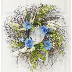 a wreath with blue flowers and greenery hanging on a white front door or wall