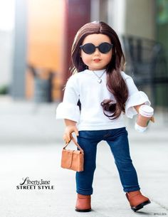 the doll is wearing sunglasses and holding a purse while standing on the sidewalk with her hands in her pockets