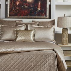 a bed with gold comforter and pillows in a bedroom next to a painting on the wall