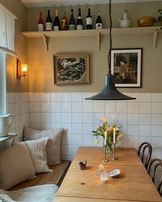 a wooden table sitting under a hanging light next to a kitchen counter with flowers on it