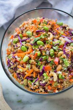 a glass bowl filled with rice, carrots, peas and other veggies