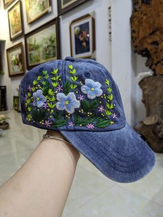 a woman's hand holding up a blue hat with flowers on it in front of pictures