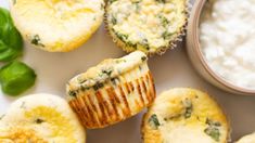 several muffins with spinach and cheese on them next to a bowl of cottage cheese