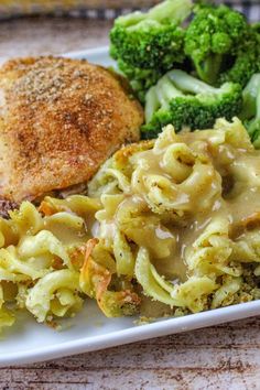 a white plate topped with pasta and meat covered in gravy next to broccoli