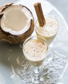 two glasses filled with drink sitting on top of a plate next to an open coconut