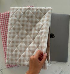 a person holding an apple laptop in front of two plaid cloths on top of a table