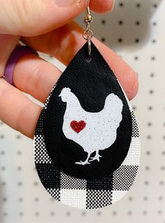 a hand holding a black and white keychain with a red heart in the shape of a chicken