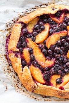 a pie with blueberries and peaches on it sitting on a piece of parchment paper