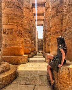 a woman sitting on the side of a stone pillar in an ancient building with writing on it