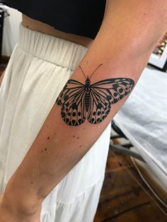 a woman's arm with a black and white butterfly tattoo on her left arm