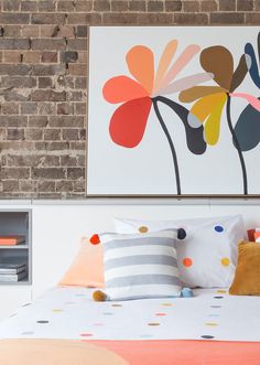 a bed with colorful pillows on it in front of a brick wall and painting above the headboard