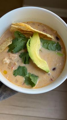 a white bowl filled with chicken tortilla soup topped with avocado and cilantro