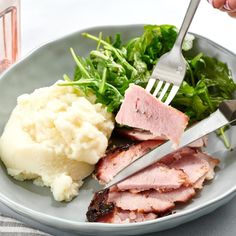 a plate with meat, mashed potatoes and greens on it is being held by a fork