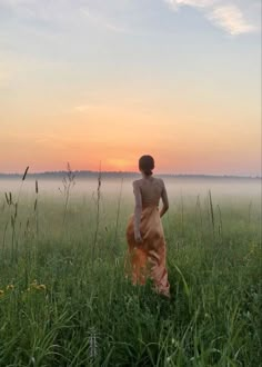 a person standing in the middle of a field with foggy sky and grass behind them