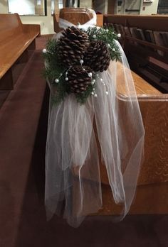 a pine cone is tied to the pews at a church with white netting and greenery