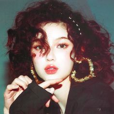 a woman with curly hair wearing large gold hoop earrings and black jacket, posing for the camera