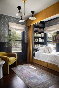 a bedroom with a bed, chair and bookshelf in the corner near two windows