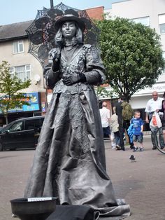 a statue of a woman holding an umbrella in the middle of a street with people walking by