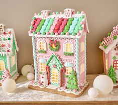 three gingerbread houses decorated with icing and decorations on top of a table next to white balls