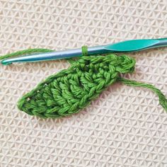 a green crochet stitch with a blue handled knitting needle on top of it