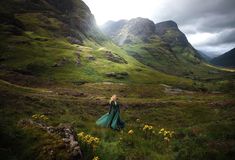 a woman in a long green dress walking through the mountains