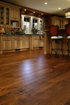 a large kitchen with wooden floors and white cabinets, along with two bar stools