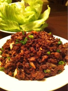 a white plate topped with meat and lettuce on top of a wooden table