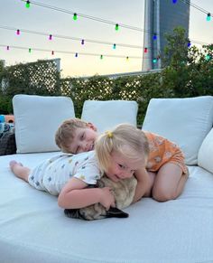 two young children cuddle on the back of a couch with a stuffed animal in front of them