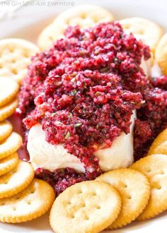 a white plate topped with crackers and cheese covered in cranberry sauce next to crackers