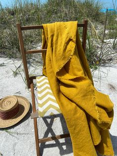 a yellow blanket sitting on top of a wooden chair next to a hat and umbrella