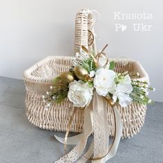 a white flower arrangement in a wicker basket with ribbon and ribbons on the side