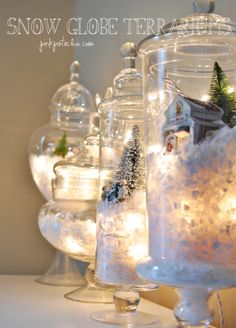 christmas decorations in glass jars with lights on the top and snow around them, along with small trees