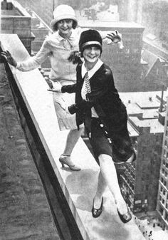 two women dressed in business attire posing on the edge of a high rise building with their arms around each other