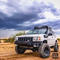 a white jeep parked on top of a dirt road under a cloudy sky with clouds