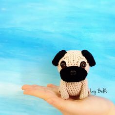 a small crocheted dog sitting on top of a person's hand in front of a blue background