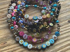 two bracelets that have letters on them and beads attached to each other, sitting on top of a wooden table