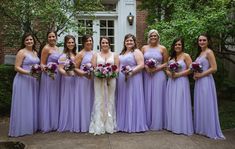 a group of women standing next to each other in front of a building holding bouquets