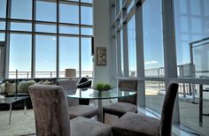 a living room filled with furniture and lots of glass windows next to a table surrounded by chairs