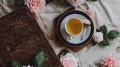 a cup of tea on a saucer next to a book and some pink flowers