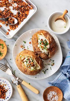 two baked potatoes on a plate next to other dishes and utensils with spoons