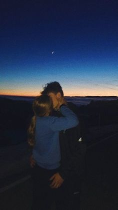 two people standing next to each other in front of the sky at night, hugging