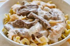 a white bowl filled with pasta covered in meat and gravy on top of a table