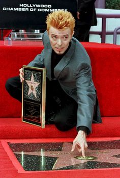 a man in a suit and tie kneeling down next to a star on the hollywood walk of fame